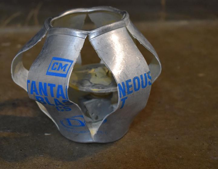 exploded CM Instantaneous Blast CS Grenade cans from defense technology are pictured with blue writing identifying the type of munition on split aluminum canister, The lids have been completely blown off and the canisters have split along 6 different seems in pre-machined grooves.