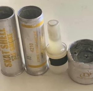 two 40 mm shells with yellow writing, one that says skat shell saf smoke, but the focal one being the next one saying 4210 40mm white smoke. also an impact baton and part of a triple chaser