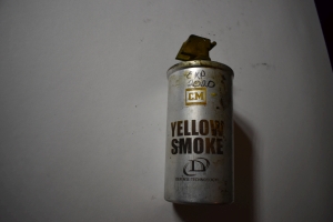 old silver spent grenade can with white  writing that says `CM yellow smoke Defense Technology`