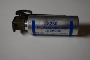 small silver grenade can with blue writing that says `8230 Tactical Grenade CS Smoke`. The cylander is plugged with the trigger mechanism. This one has it's lever and fuse ring in tact as it has not been used..