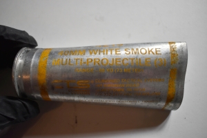 40 mm shell with yellow writing, 40mm white smoke multi projectile (3). a hand with a black nitrile glove holds it