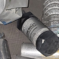 black grenade with a grey label and black and white  writing that says `Low Roll Distraction Device Defense Technology` sitting on a car seat with other munitions behind it