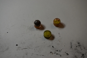 3 fn303 rounds are pictured with yellow paint, some are intact and some just pieces of broken plastic casings, but horrible bismuth beads are seen up front in the intact balls. They look a lot like pepper balls, round and plastic, two halves snapped together like sinister Easter Eggs, but the have stabilizers on the bottom to direct their impact. Rough plastic with channels for aerodynamic performance.