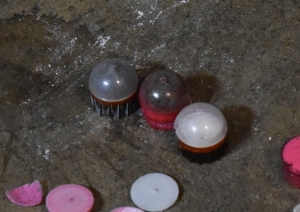 fn303 rounds are pictured, some are intact and some just pieces of broken plastic casings, but horrible bismuth beads are seen up front in the intact balls. They look a lot like pepper balls, round and plastic, two halves snapped together like sinister Easter Eggs, but the have stabilizers on the bottom to direct their impact. Rough plastic with channels for aerodynamic performance.