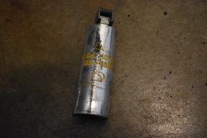 An old, small, silver grenade canister is pictured with yellow writing that says `TD Pocket Tactical SAF Smoke`, the aluminum canister is nearly 5 inches long but only about an inch and a half in diameter. The trigger mechanism is black plastic, with a long plastic compression arm. The security ring is missing from the smoke grenade, because it's been used.
