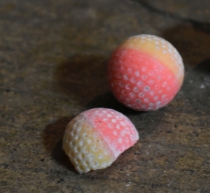 Small dimpled spheres that resemble golf balls are pictured on the ground. Their paint colors vary, but the ones pictured are red and a gradient of white to yellow to Orange to pink and red. These dimples function to make the spheres noticeably more aerodynamic when propelled. They're made of a smooth plastic like substance that appears hard to the touch. Much like a smaller golf ball.
